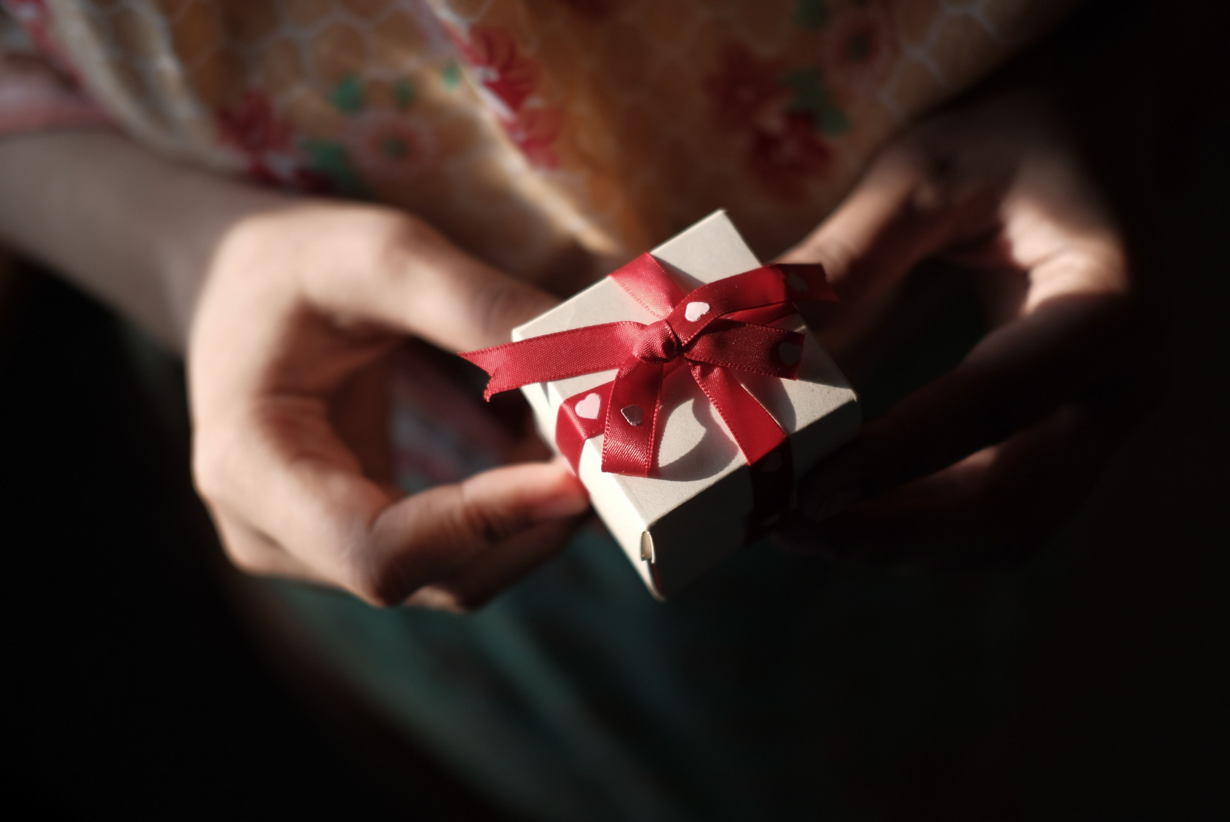 Handen die een ingepakt cadeautje met rode strik aangeven